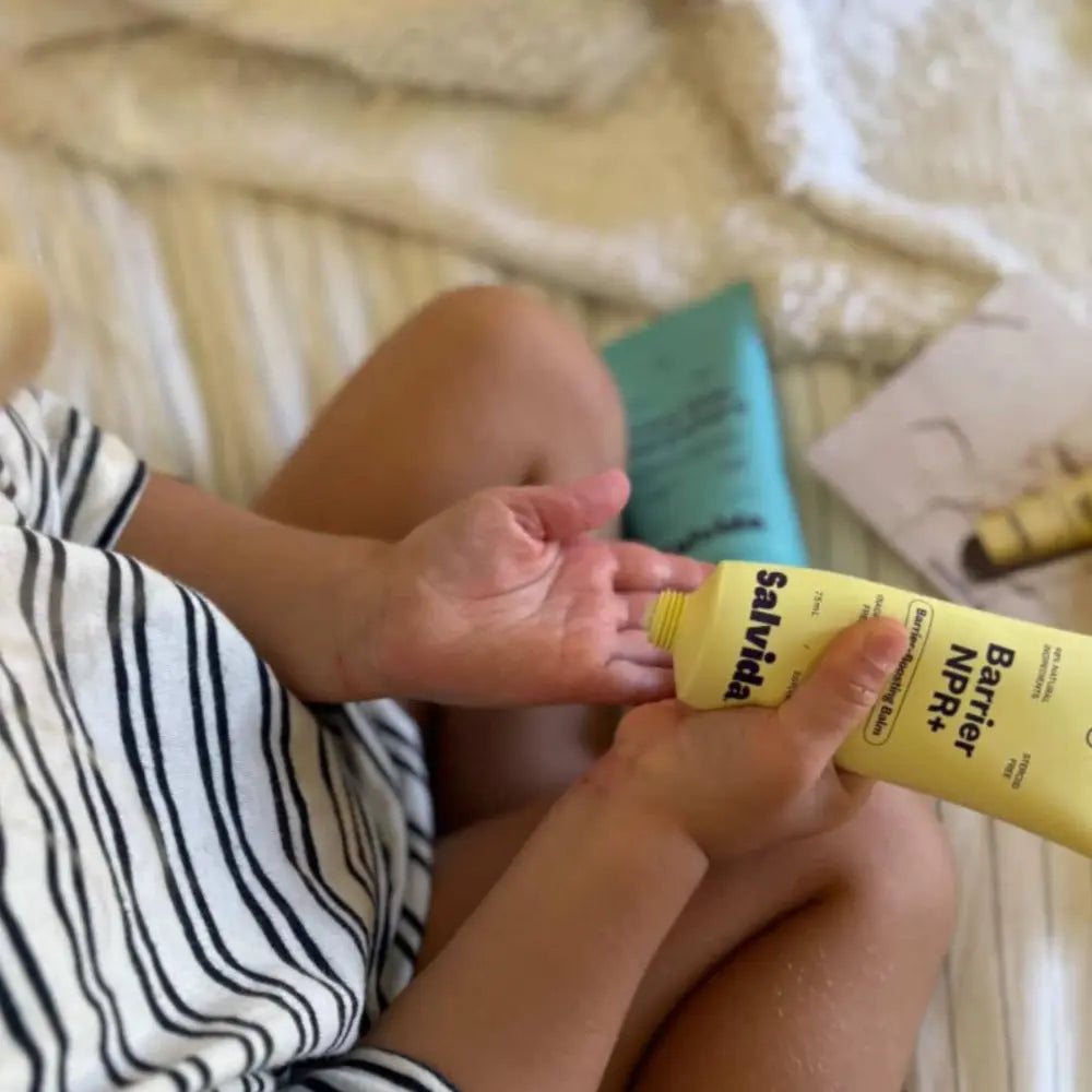 Person applying lotion to their hand with a yellow tube labeled 'NPR' on a textured surface.