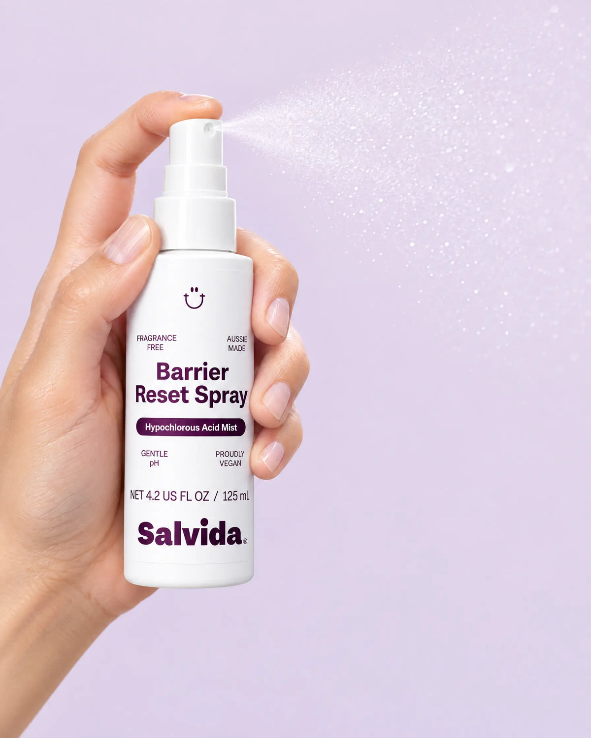 Photo of a hand holding and spraying Salvida Barrier Reset Spray against a lilac background