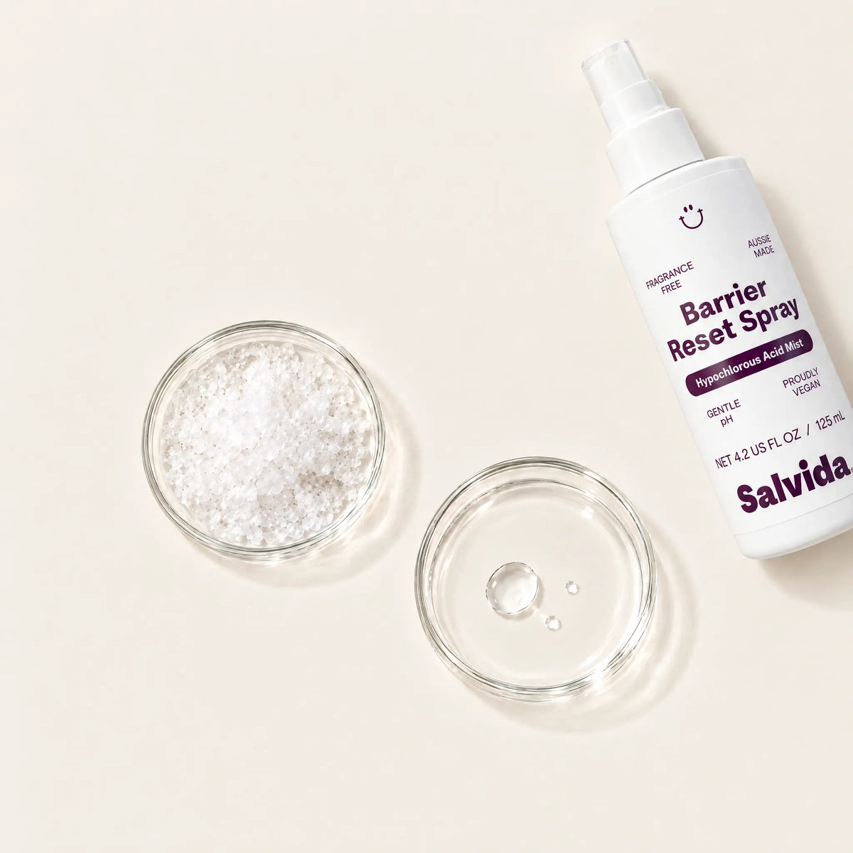Salvida Barrier Reset Spray bottle beside two glass dishes, one holding a white gel texture and the other a clear liquid